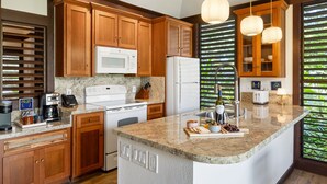 A kitchen with wooden cabinets, a microwave, stove, refrigerator, and a granite countertop.
