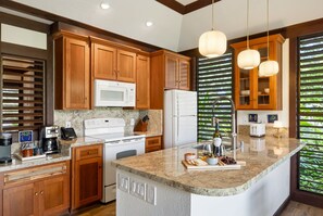 A kitchen with wooden cabinets, a microwave, stove, refrigerator, and a granite countertop. - Kiahuna #44 • A/C • REMODELED & UPDATED Ground-Floor End Unit • 2 Min to Beach (Koloa)