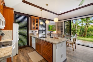 A modern kitchen with wooden cabinets, a built-in island, and a large window overlooking a garden. - Kiahuna #44 • A/C • REMODELED & UPDATED Ground-Floor End Unit • 2 Min to Beach (Koloa)