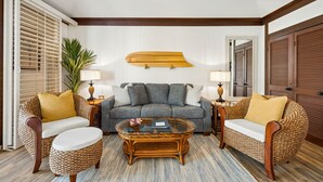 A living room with a sofa set, a coffee table, and a surfboard mounted on the wall. - Kiahuna #44 • A/C • REMODELED & UPDATED Ground-Floor End Unit • 2 Min to Beach (Koloa)