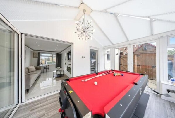 A pool table in a modern room with large windows and a sliding glass door leading to a living area.