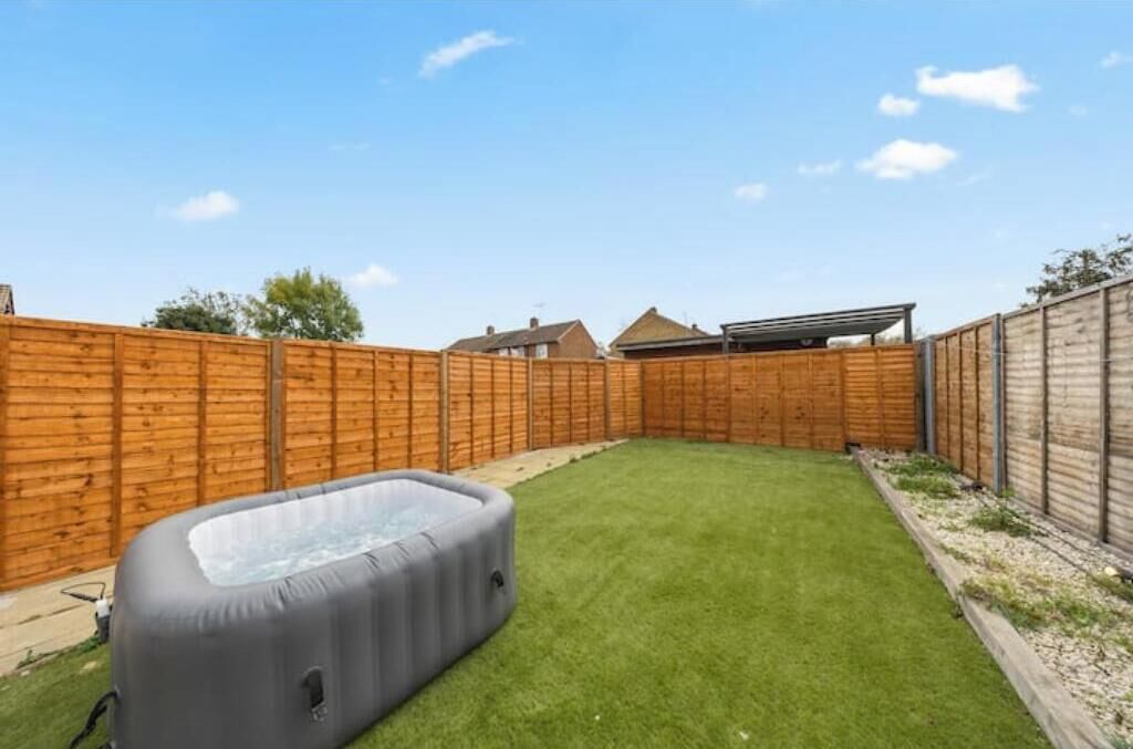 A backyard with a wooden fence, a hot tub, and a grassy lawn.