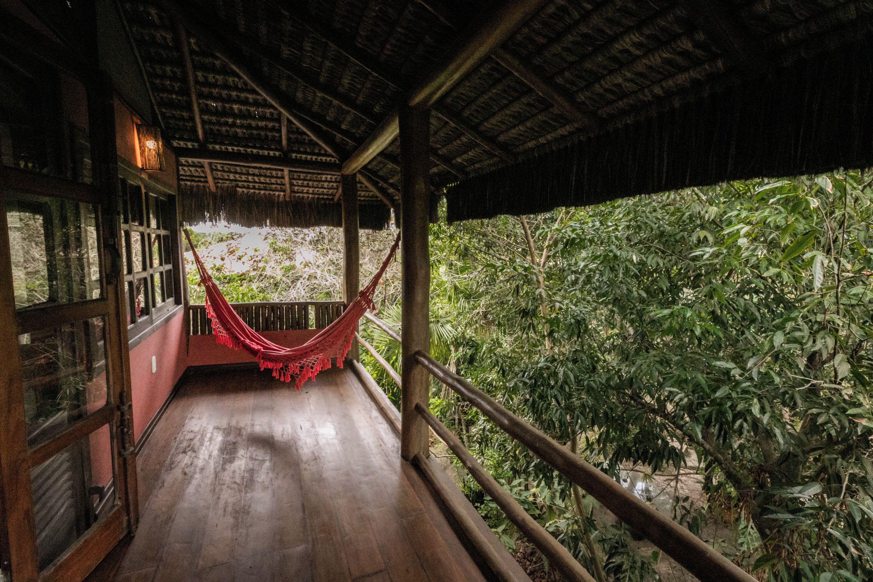 A wooden deck with a hammock, wooden railings, and a view of dense greenery.