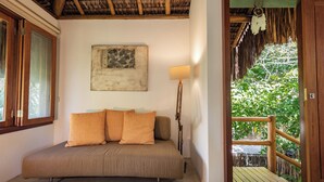 A room with a sofa, a lamp, a painting, and a view of greenery through a doorway. - Pousada Colmeia (Santa Cruz Cabrália)