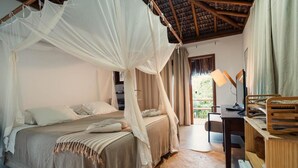 A bedroom with a canopy bed, a desk with a lamp, and a view of greenery outside. - Pousada Colmeia (Santa Cruz Cabrália)