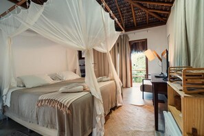 Ein Schlafzimmer mit Baldachinbett, Schreibtisch mit Lampe und Blick auf Grünfläche.