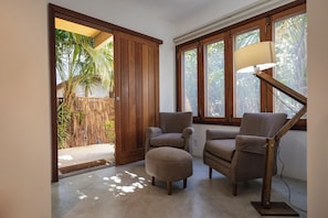 A room with a sliding door leading to a covered outdoor area, two armchairs, a side table, and a floor lamp. - Pousada Colmeia (Santa Cruz Cabrália)