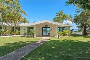 Une maison moderne avec une grande porte d’entrée, une allée pavée et des palmiers.