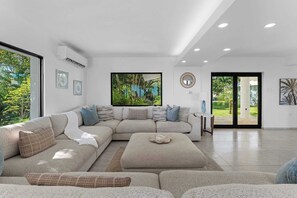 Un salon moderne avec un canapé d’angle, une table basse et une grande fenêtre donnant sur un paysage verdoyant.