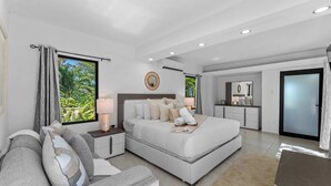 Une chambre moderne avec un grand lit, des tables de chevet, un canapé et une vue sur la verdure.