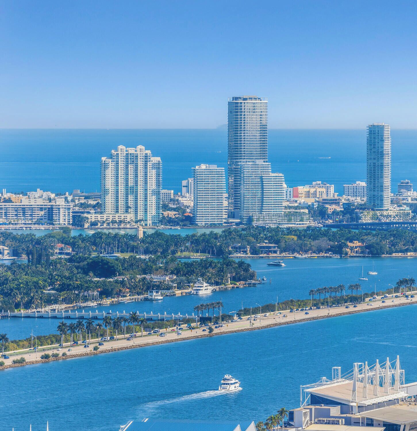 A coastal cityscape with high-rise buildings, a marina, and a bridge.