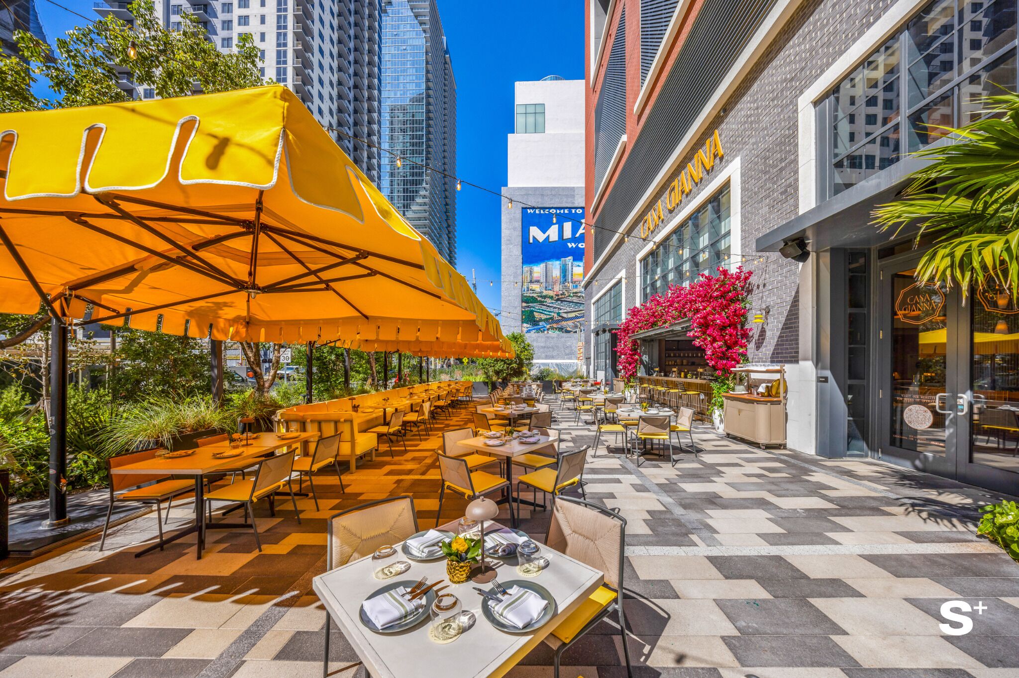 An outdoor dining area with tables and chairs, a large yellow umbrella, and a building with a sign that reads 'CINNABBA.'