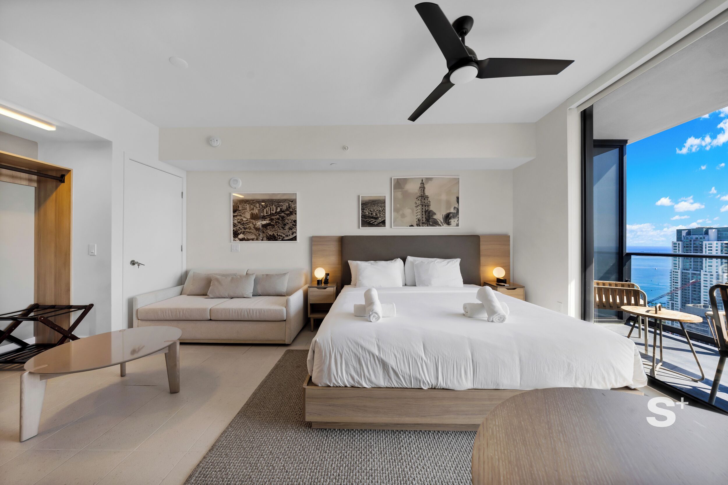 Ein modernes Hotelzimmer mit Bett, Sofa, Schreibtisch und einem Balkon mit Blick auf die Stadt.