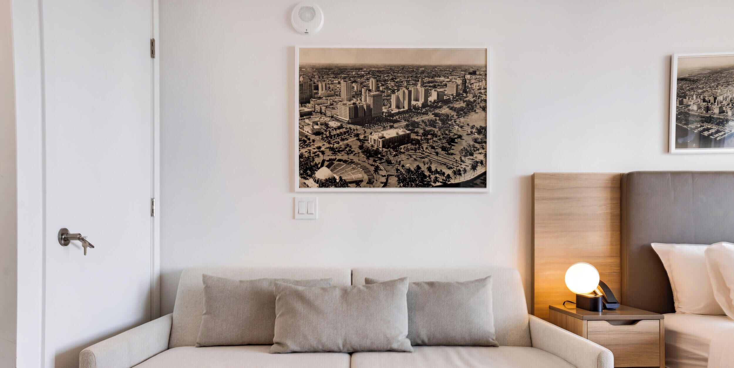 Een moderne hotelkamer met een stadsfotografie aan de muur, een bank, een nachtkastje met een lamp en een houten hoofdbord.
