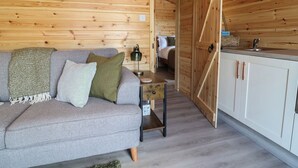 Interior acogedor de una cabaña con sofá, una mesita, lámpara y una zona de cocina con armarios.