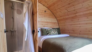 Un dormitorio acogedor con paredes de madera, una cama, almohadas y una zona de ducha.
