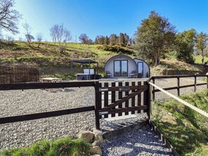 Una cabaña rústica con una zona de estar al aire libre cubierta, un camino de entrada de grava y una valla de madera.