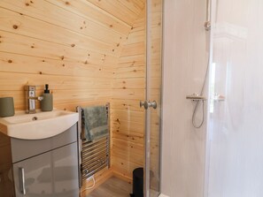 Un baño con pared de madera, lavamanos con espejo, toallero y zona de ducha.