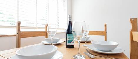 Una mesa de comedor con platos blancos, cuencos, copas de vino y una botella de vino.