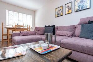 Ein Wohnzimmer mit zwei Sofas, einem Couchtisch, einer Zeitschrift und einem Fenster mit Jalousien.