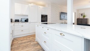 Una cocina moderna con muebles blancos, encimera de mármol y una pared de ladrillo decorativa.