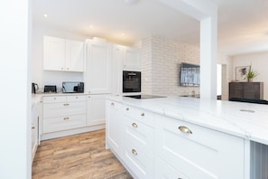 A modern kitchen with white cabinetry, a marble countertop, and a brick accent wall.