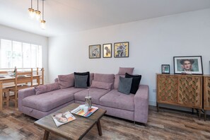 A living room with a purple sofa, wooden coffee table, and a dining area with a wooden table and chairs.