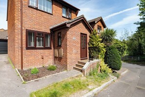 A two-story brick house with a front porch, a small garden, and a clear sky. - Open Mind Property - Hot Tub Retreat Sleeps 9 (Bournemouth)