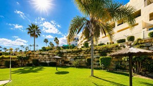 A well-maintained outdoor area with a stone wall, palm trees, and a thatched umbrella. - Arenal Golf, with private garden, swimming pool, BBQ (Benalmádena)