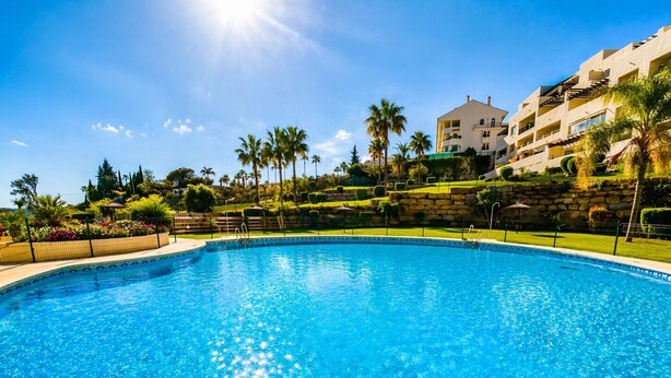 A clear blue swimming pool surrounded by a well-maintained garden with palm trees and a stone wall. - Arenal Golf, with private garden, swimming pool, BBQ (Benalmádena)