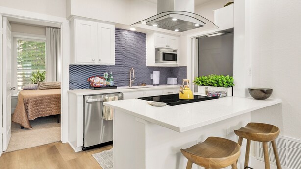A modern kitchen with white cabinetry, a black backsplash, and a central island with stools. - The Cove:2 bdrm, 4 minute walk to A&M (College Station)