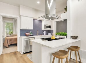 Una cocina moderna con armarios blancos, un salpicadero negro y una isla central con taburetes.