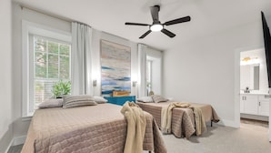 A bedroom with two beds, a ceiling fan, a painting, and a bathroom with a mirror and cabinets. - The Cove:2 bdrm, 4 minute walk to A&M (College Station)