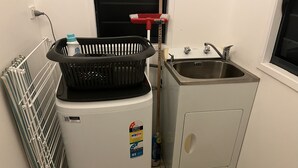 A compact kitchen with a washing machine, a sink, and a radiator. - Toreaiva 91 Beachfront Studio - Upper (Arorangi)