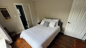 Une chambre avec un grand lit, une porte, une chaise et un plancher en bois.