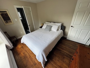 Ein Schlafzimmer mit einem großen Bett, einer Tür, einem Sessel und Holzboden.