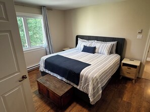 A bedroom with a bed, a nightstand, a wooden chest, a window with curtains, and a thermostat on the wall. - Getaway to Mahone Bay Nova Scotia (Mahone Bay)