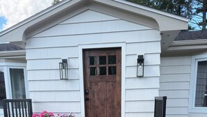 Une maison avec une porte d’entrée en bois, deux plantes en pot et un escalier en bois menant à l’entrée.