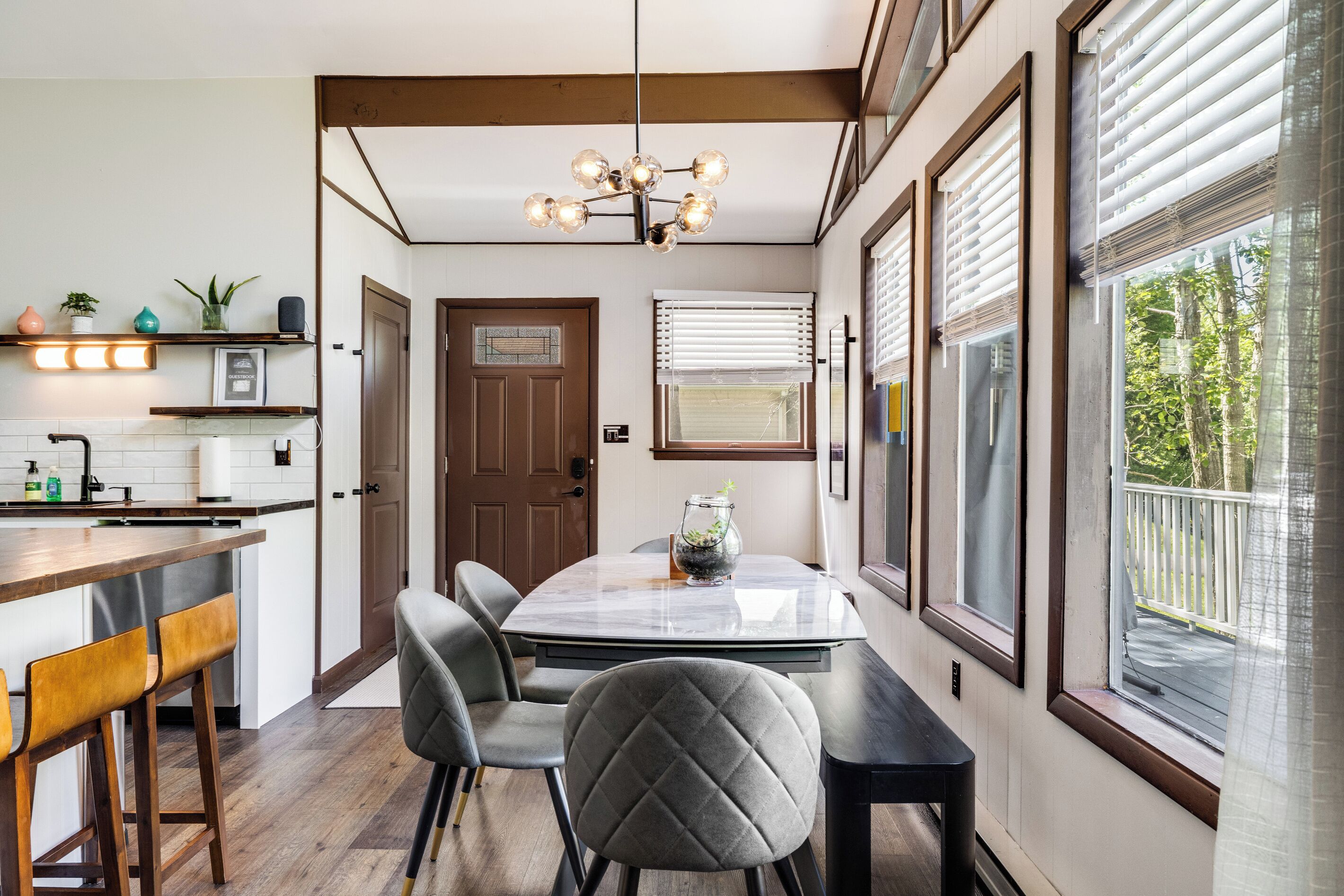 A modern kitchen with a dining area, wooden beams, a chandelier, and large windows.