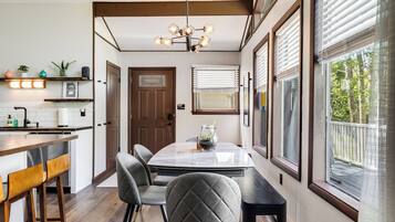 A modern kitchen with a dining area, wooden beams, a chandelier, and large windows.