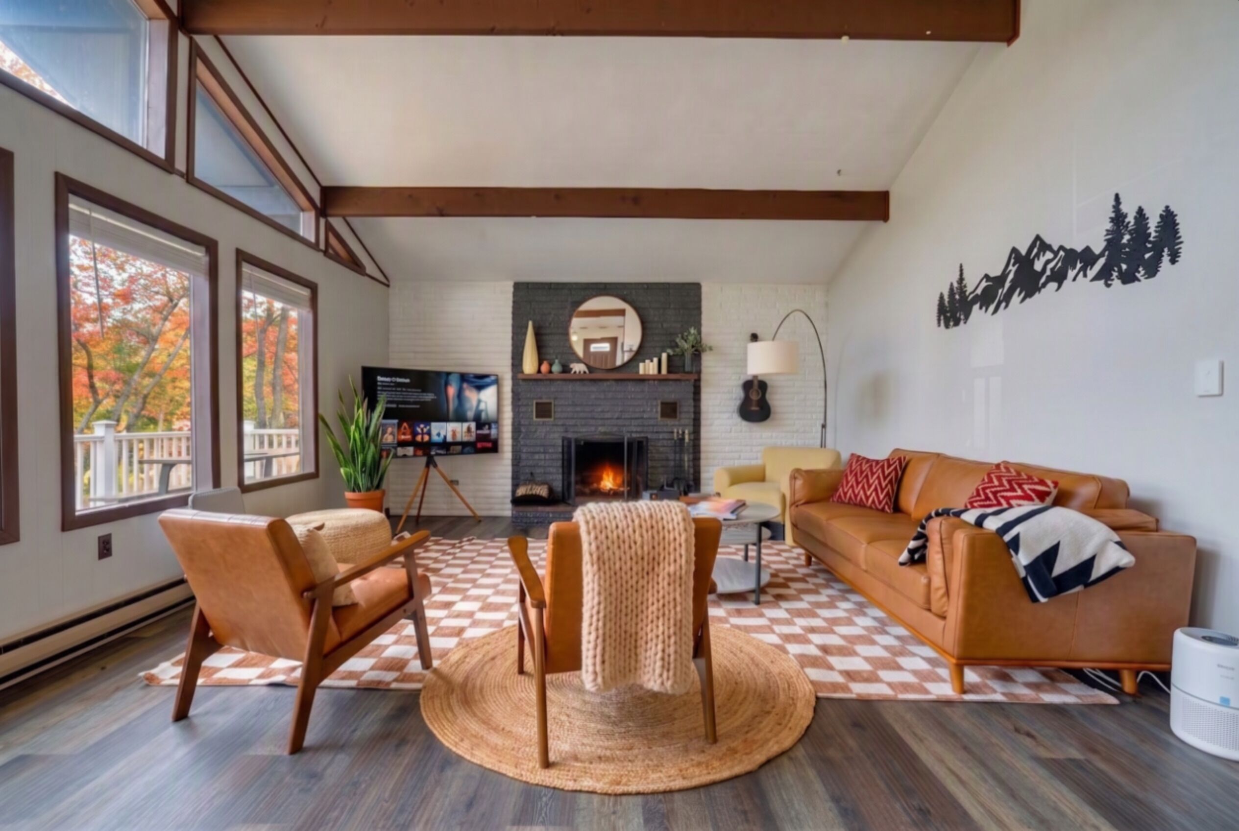 Una sala de estar con chimenea, un sofá, un televisor y un ventanal con hojas otoñales.