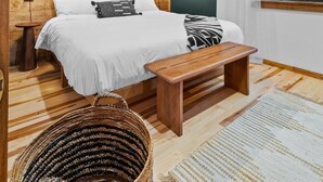 Une chambre à coucher avec une tête de lit en bois, un grand lit, des lampes de chevet, un panier en osier et une vue sur les arbres par la fenêtre.