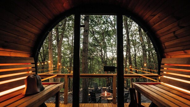 Une cabane en bois dotée d’une terrasse, de bancs, d’un foyer et de guirlandes lumineuses.