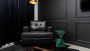 A dark-themed room with a leather sofa, a green patterned side table, and a wall-mounted TV. - Lovely 1-bedroom studio with AC in Phoenix (Phoenix)
