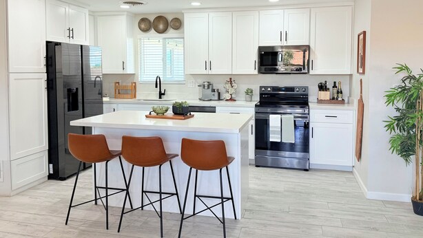 A modern kitchen with white cabinets, a black refrigerator, a stainless steel oven, and a central island with bar stools. - 4BR Family & group Oasis in Mesa – Big Backyard & Steps from Sloan Park & ASU!! (Mesa)
