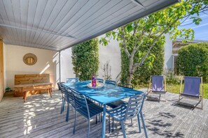 An outdoor patio with a blue table and chairs, a wooden bench, and a covered area with a white ceiling. - Maison Côté Bassin – Abatilles (Arcachon)
