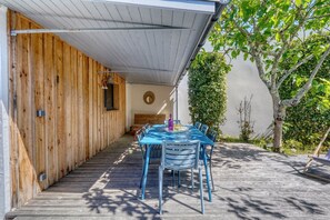 A covered outdoor seating area with a wooden deck, a table with chairs, and a bench. - Maison Côté Bassin – Abatilles (Arcachon)