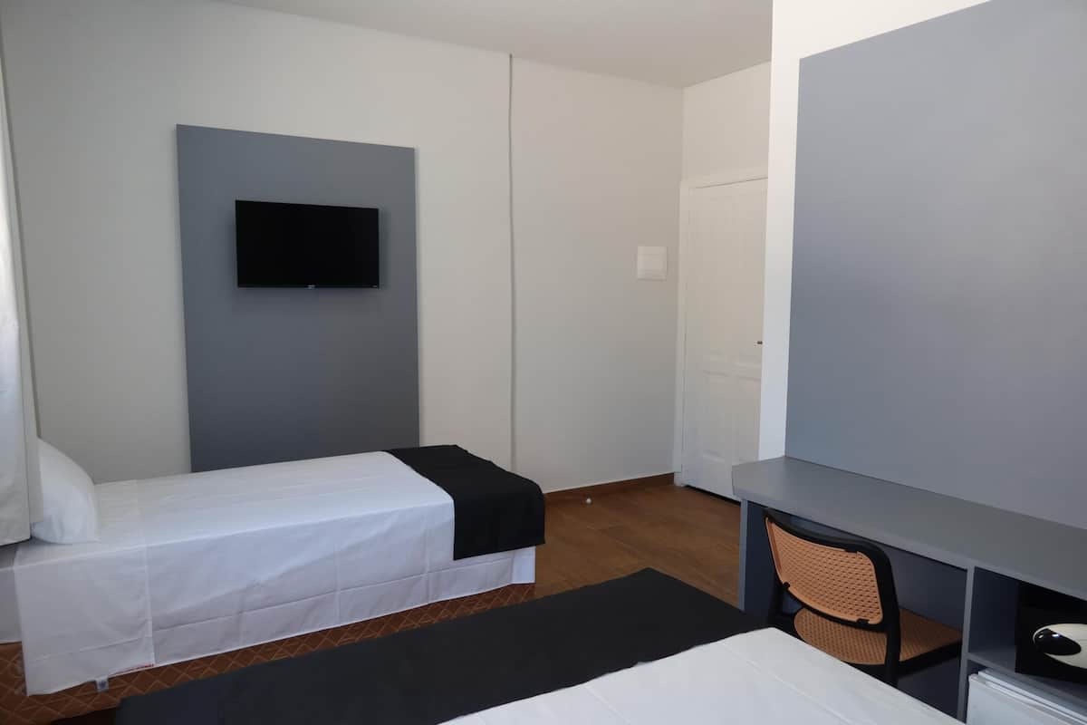Une chambre d’hôtel comprenant un lit, un bureau, une chaise, un téléviseur à écran plat fixé au mur et une armoire.