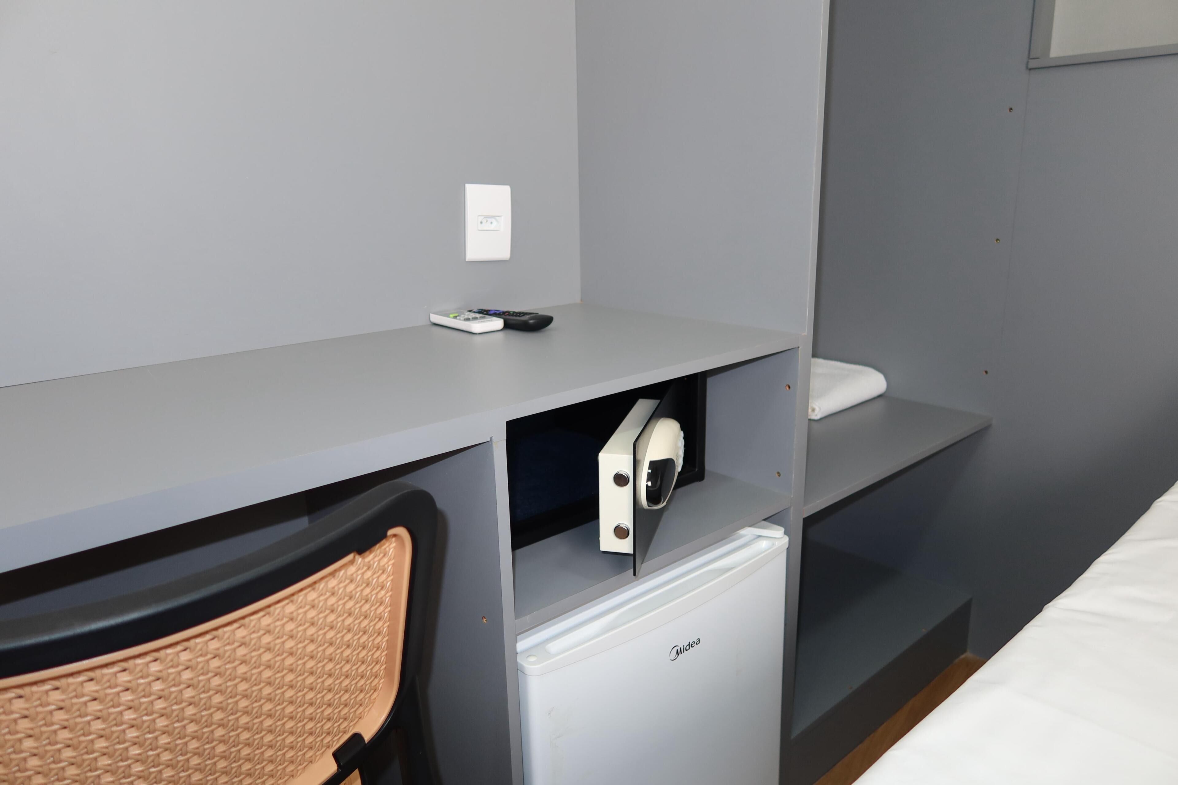 A compact hotel room with a small desk, a chair, a mini-fridge, and a bed.