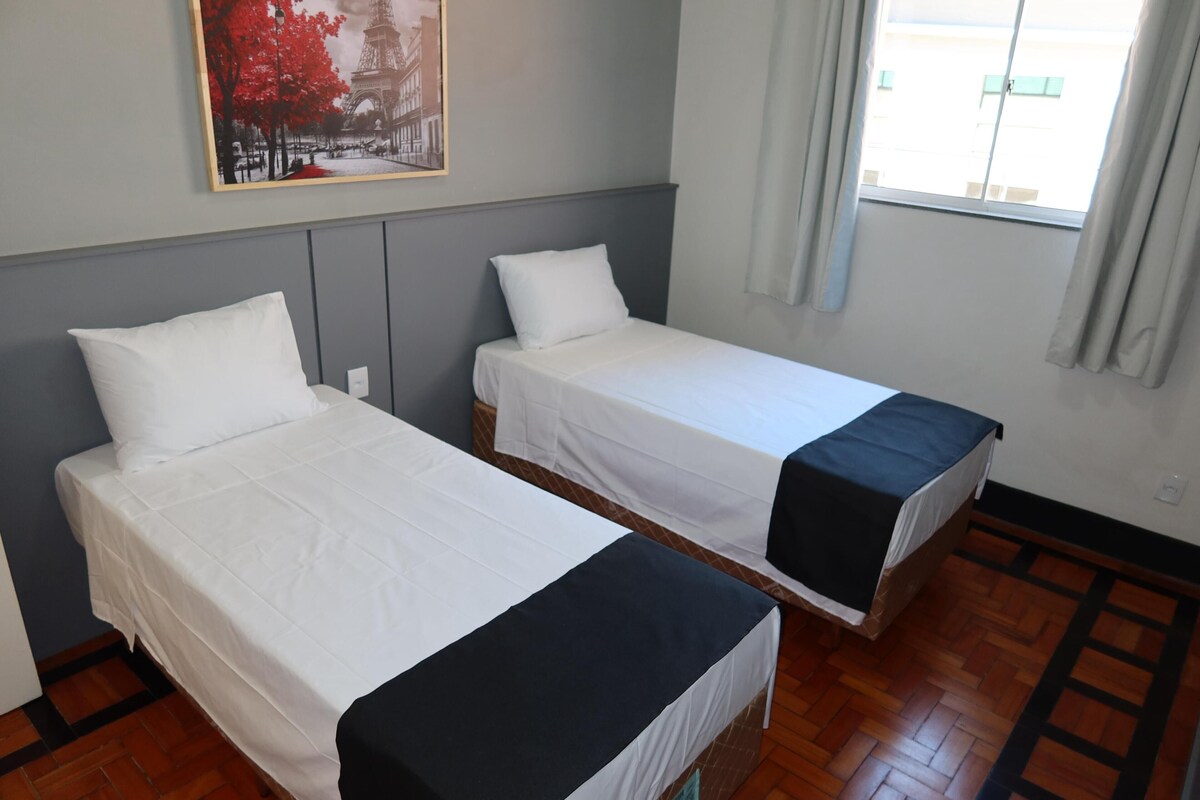 Een kamer met twee bedden, een schilderij van de Eiffeltoren, een raam met gordijnen en een houten vloer.